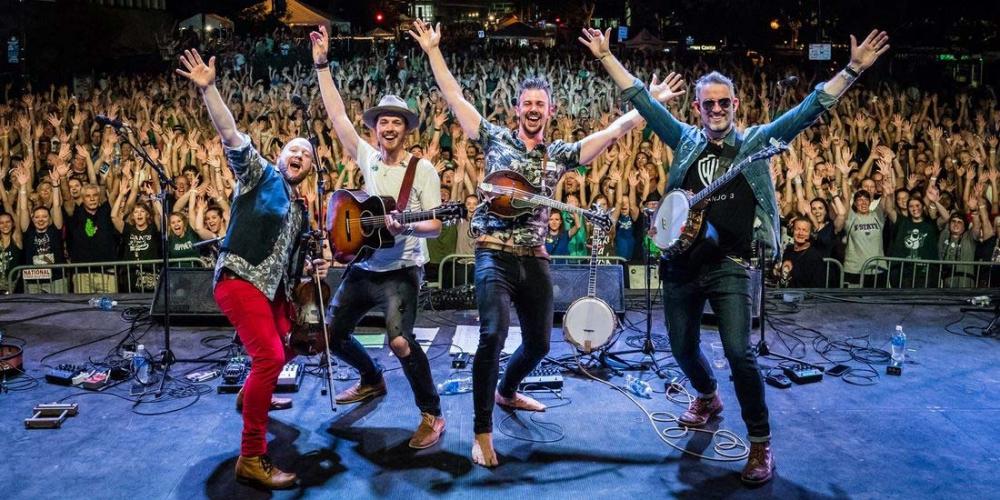  With hands in the air, We Banjo 3 faces the back of the stage with audience in background