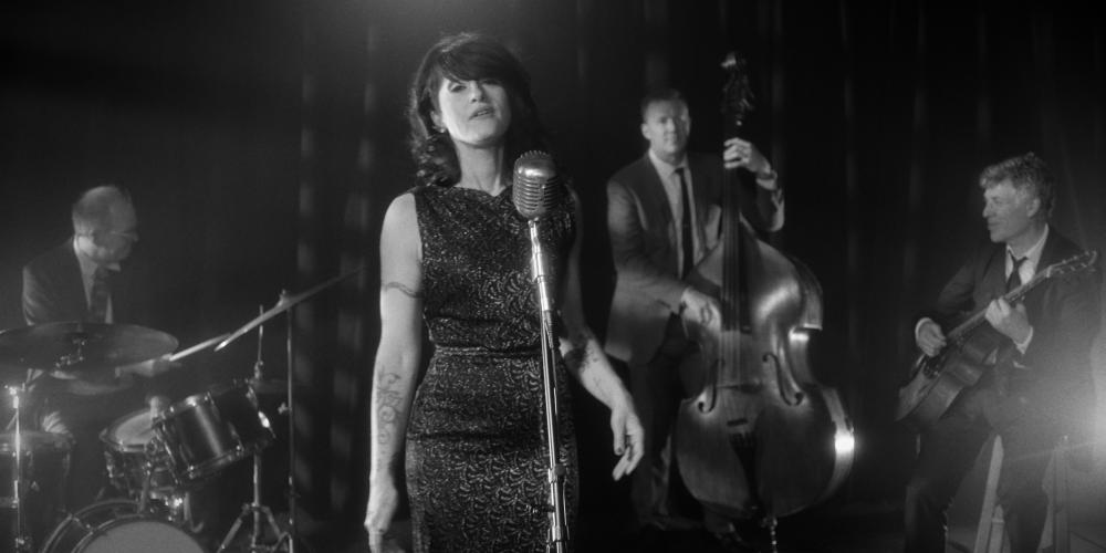 Sasha Dobson standing at a microphone singing with a band behind her