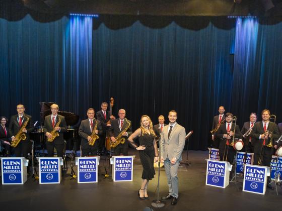 Formal photo of the Glenn Miller Orchestra on stage with the lead female singer and male band director