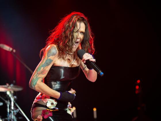 woman with long brown hair wearing a tight black strapless top singing into a microphone