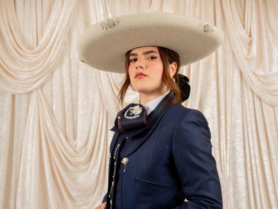 Woman posing in navy blue traje de charro outfit with a cream colored hat