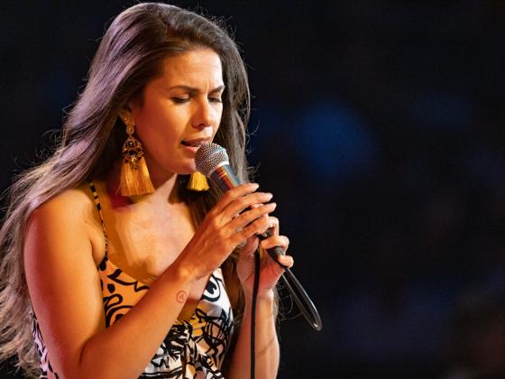 Brazilian vocalist Caro Pierotto singing on dark stage with mic in her hands