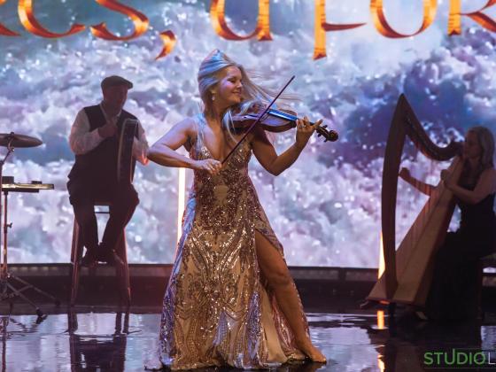 Celtic Spells Featuring Máiréad Nesbitt on stage performing on fiddle wearing a golden dress