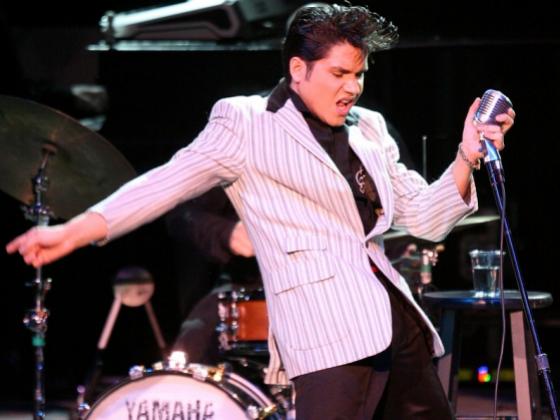 Man in a striped white suit and black pants swaying his hips to the side while holding a microphone