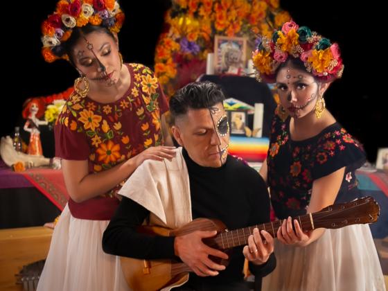 Three people pose with their faces painted with skeletons - two women and a man playing guitar