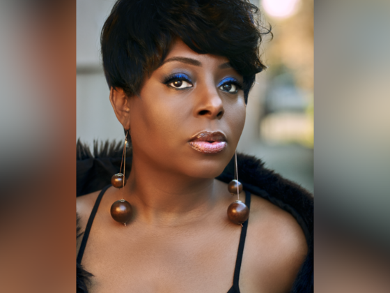 Close headshot of woman with short hair, blue eyeshadow, long earrings and black cover