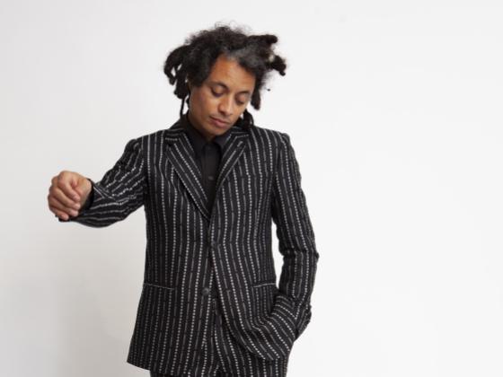 Black man with dreadlocks standing in a black suit with white pinstripes