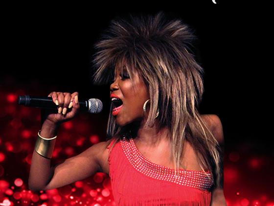 Dark skinned woman with big spikey hair singing into a microphone