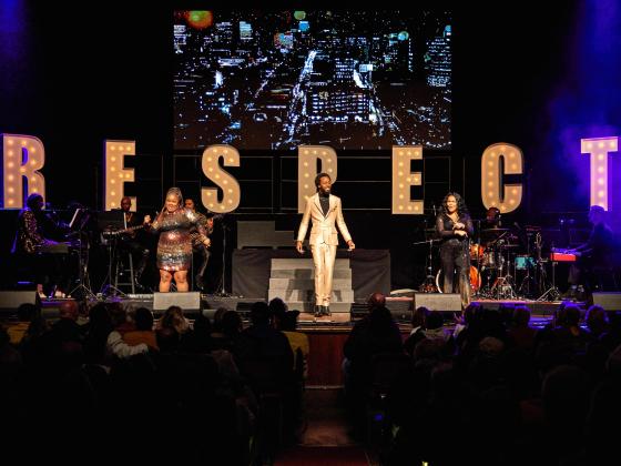 three singers performing on stage in front of large letters spelling out RESPECT