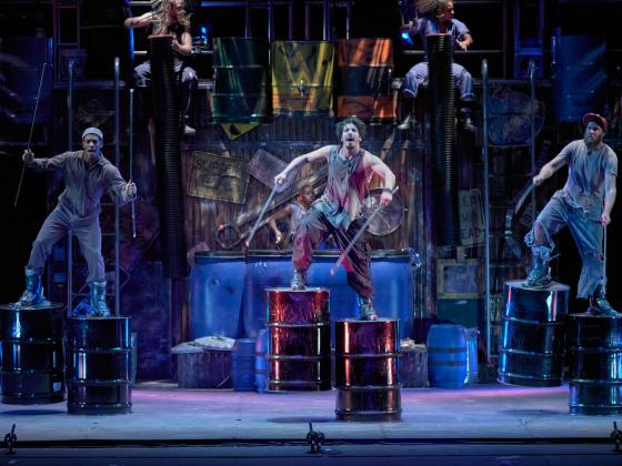 Cast members of STOMP on stage dancing with 55 gallon oil drums attached to their feet