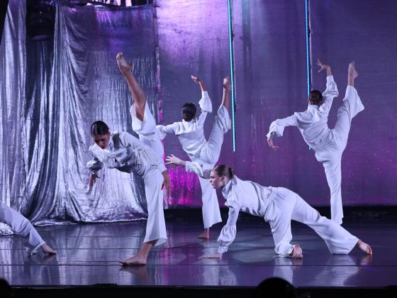 dancers dressed in white on stage with purple backlit set