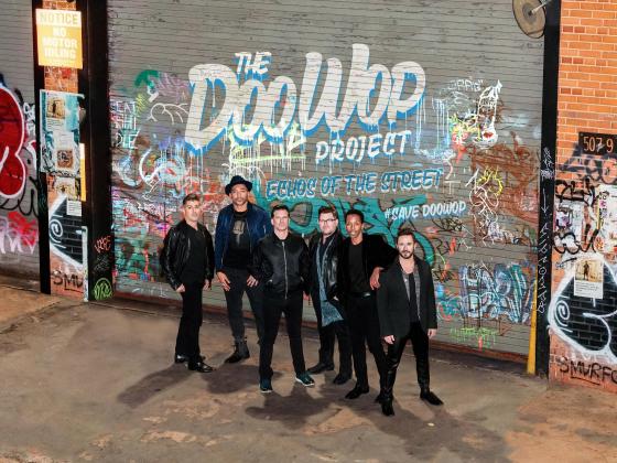 Six men standing in front  of a graffiti wall.