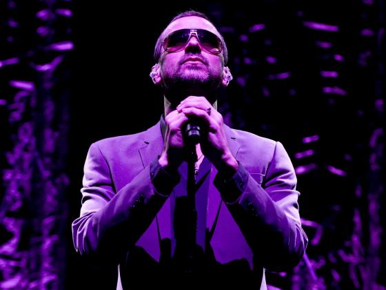 On stage wearing a purple jacket and wearing sunglasses