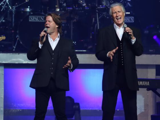 two older men in suits with gray and brown hair singing on stage
