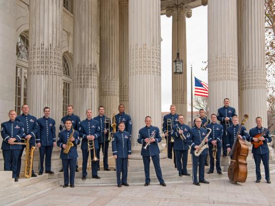 18 men in dress blues pose with their instruments