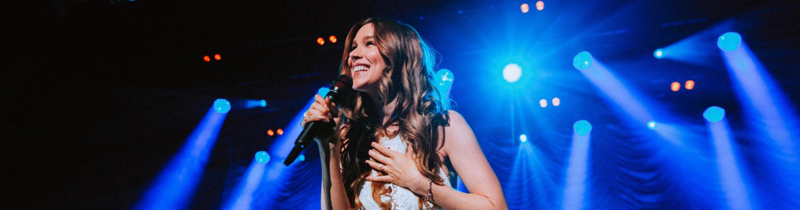 Joss Stone in white dress with blue stage light beaming behind her