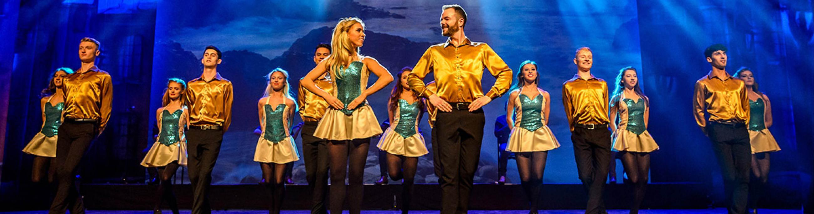 Irish step dancers wearing yellow shirts dance in front of a blue background