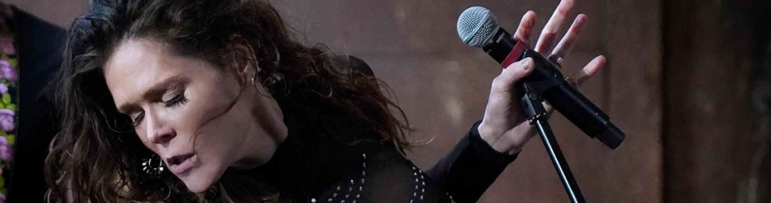 woman standing at a microphone wearing all black and looking away