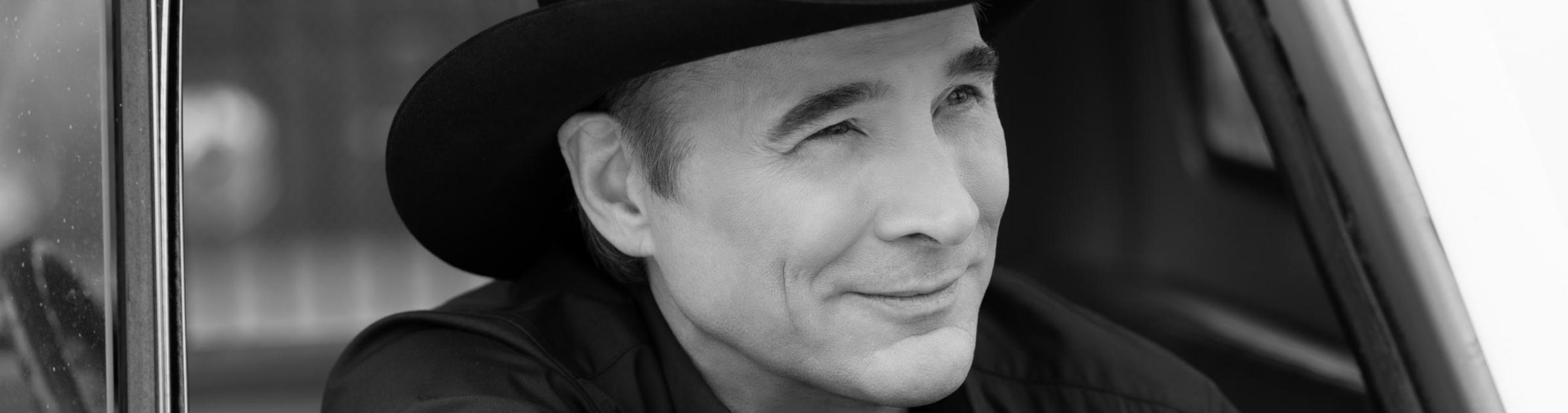 white man with black hat in black and white photo looking outside a car window