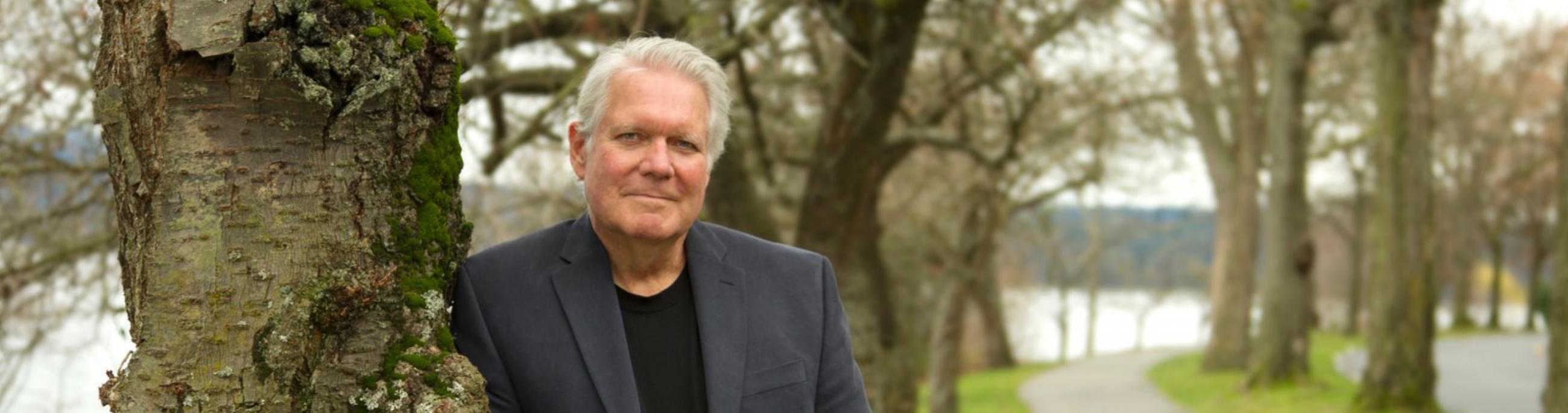 Paul Green poses outdoors, leaning on a tree.