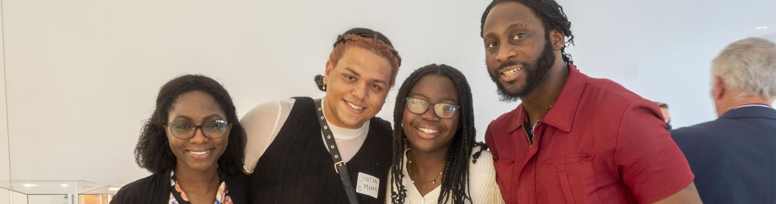 Four people pose, arm in arm, smiling at the camera