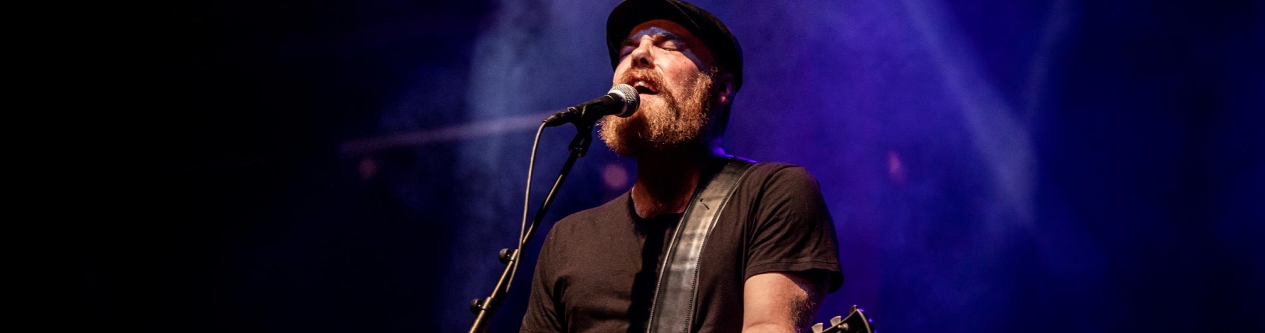 man with a beard in the spotlight singing into a microphone