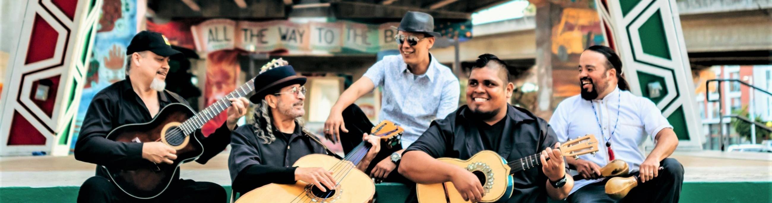 five men with instruments sitting on steps, smiling and looking at each other