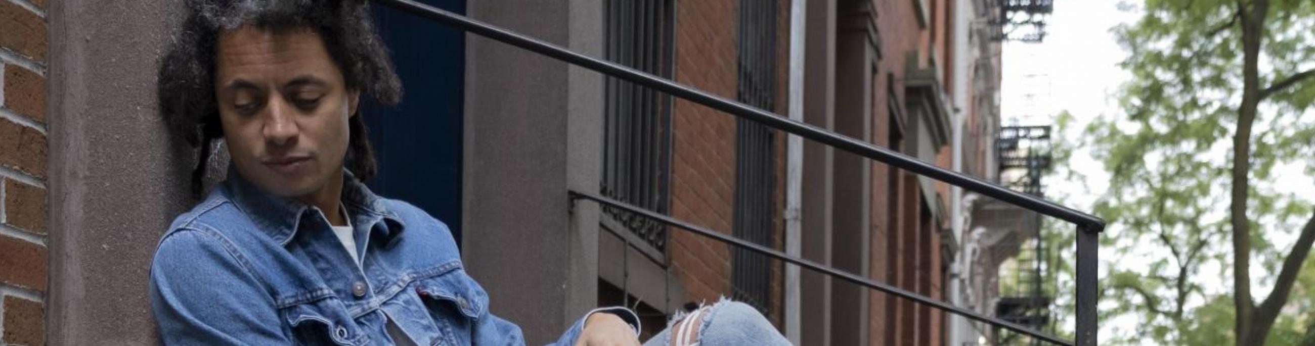 man with dreads sitting on a cement wall looking down