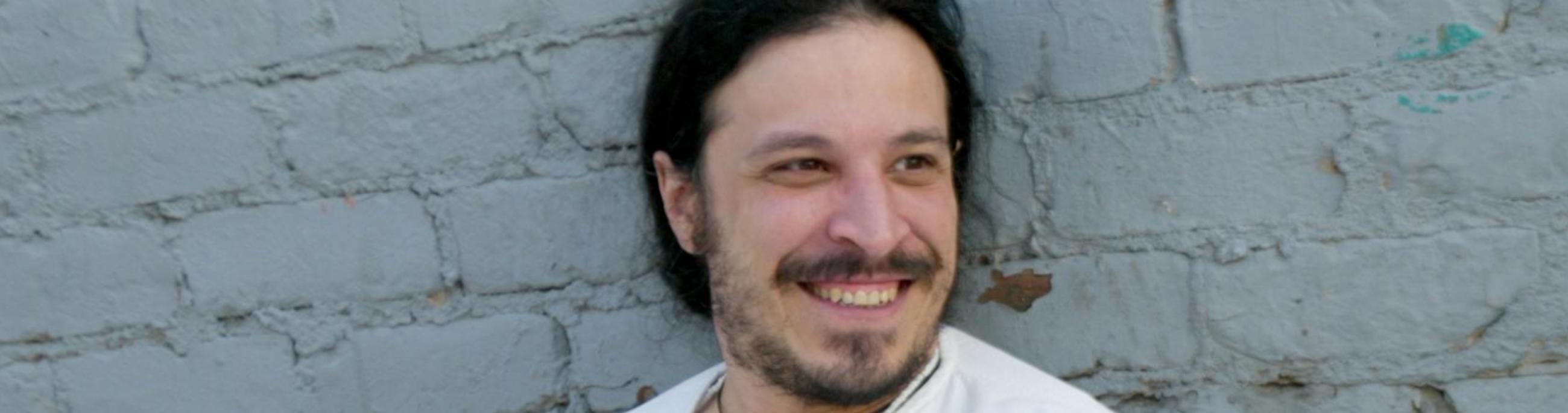 Leon Santiago, wearing a white shirt and white pants, leans back against a white brick wall.