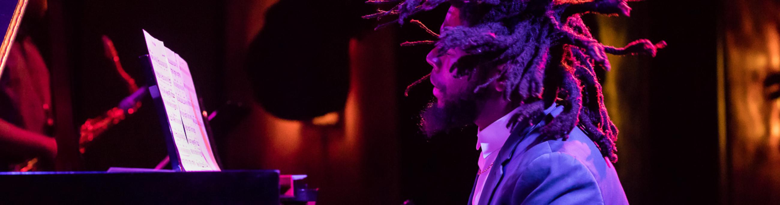 man with dreads playing the piano. the shot is taken from the left of him, making him in profile