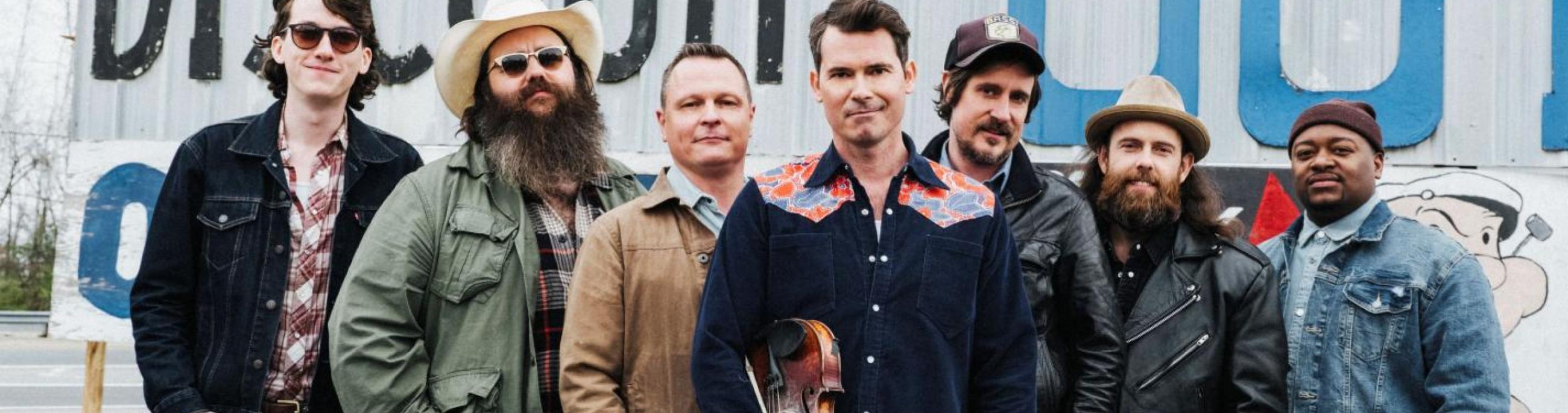 seven men standing in jeans and shirts and cowboy hats looking at the camera