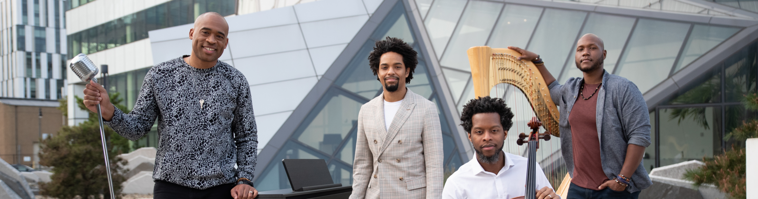 Four artists stand with their string instruments in front of a modern building