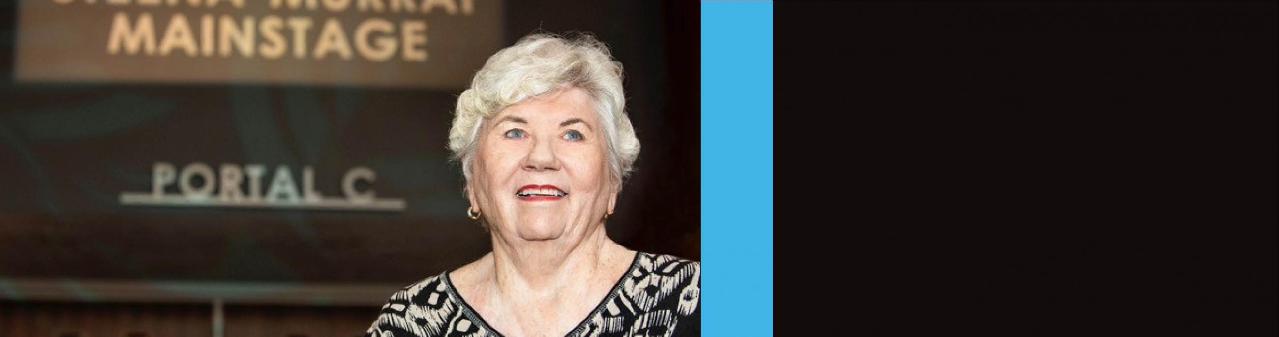 A woman with silver hair and blue eyes smiles in front of Portal C at the theatre