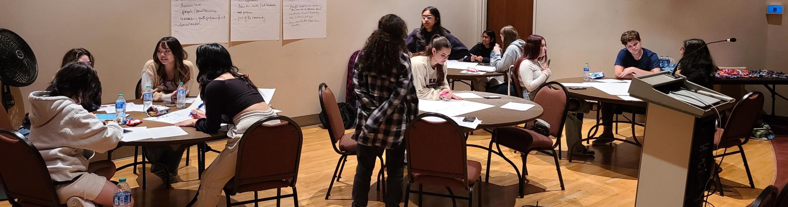 Students work around tables, talking and making notes about a project