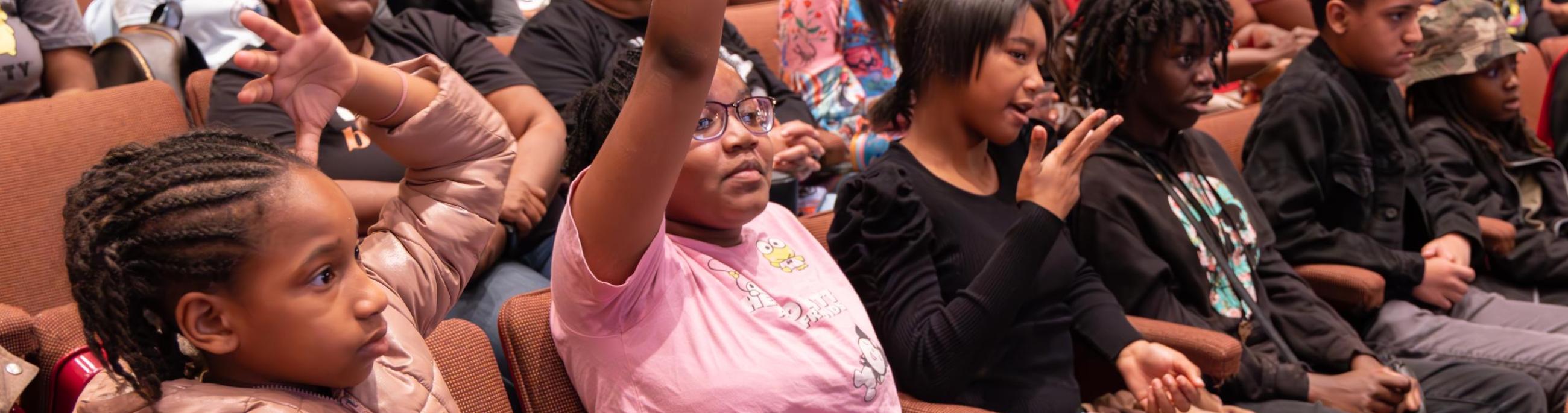 students in theatre seats with one raising their hand