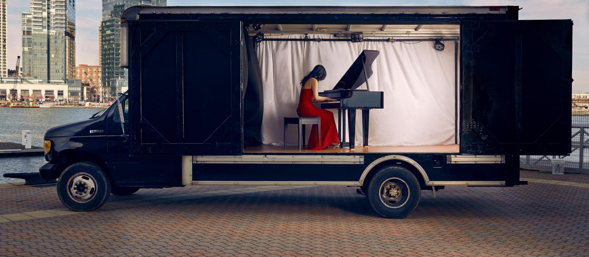 pianist in red dress playing piano inside of a truck