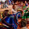 Brightly dressed dancers flourish their traditional Mexican dance skirts in front of a stage