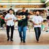 Five men walk through a courtyard toward the camera, four hold instruments