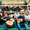 Five men sit on green stairs, some of them holding string instruments.