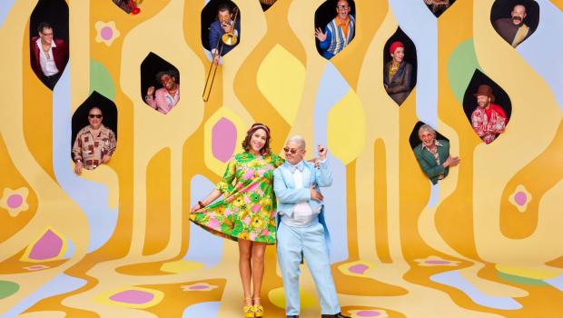 two people standing in front of a yellow background with lots of holes cut out and people sticking their heads out of the holes