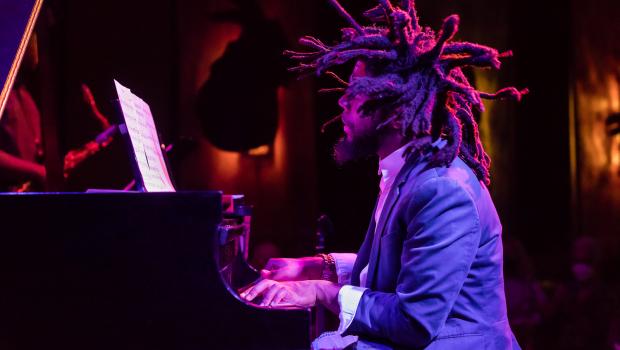 man with dreads playing the piano. the shot is taken from the left of him, making him in profile