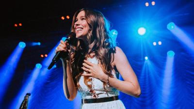 Joss Stone in white dress with blue stage light beaming behind her