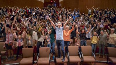 An entire audience of adults and youth are standing up and yelling jubiliantly