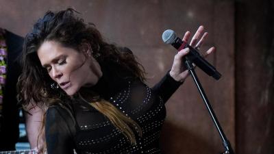 woman standing at a microphone wearing all black and looking away