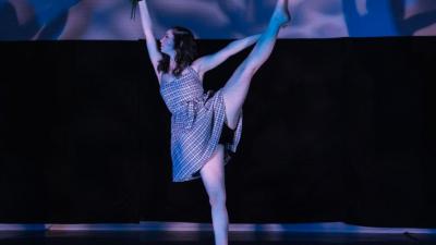 A dancer in a white dress gracefully extends one leg skyward.