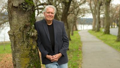 Paul Green poses outdoors, leaning on a tree.