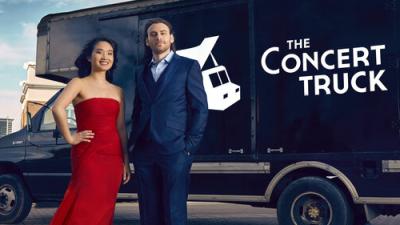 Black cargo van with the words The Concert Truck on it. A woman in a red gown and man in blue suit stand in front. 