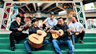 five men with instruments sitting on steps, smiling and looking at each other