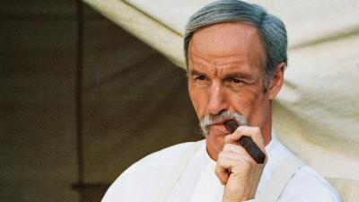 Wyatt Earp smokes a cigar while reclining in a tent.