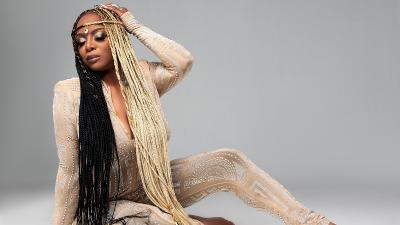 woman with half blonde half black dreadlocks, wearing a light golden jumpsuit, sitting on the ground posing